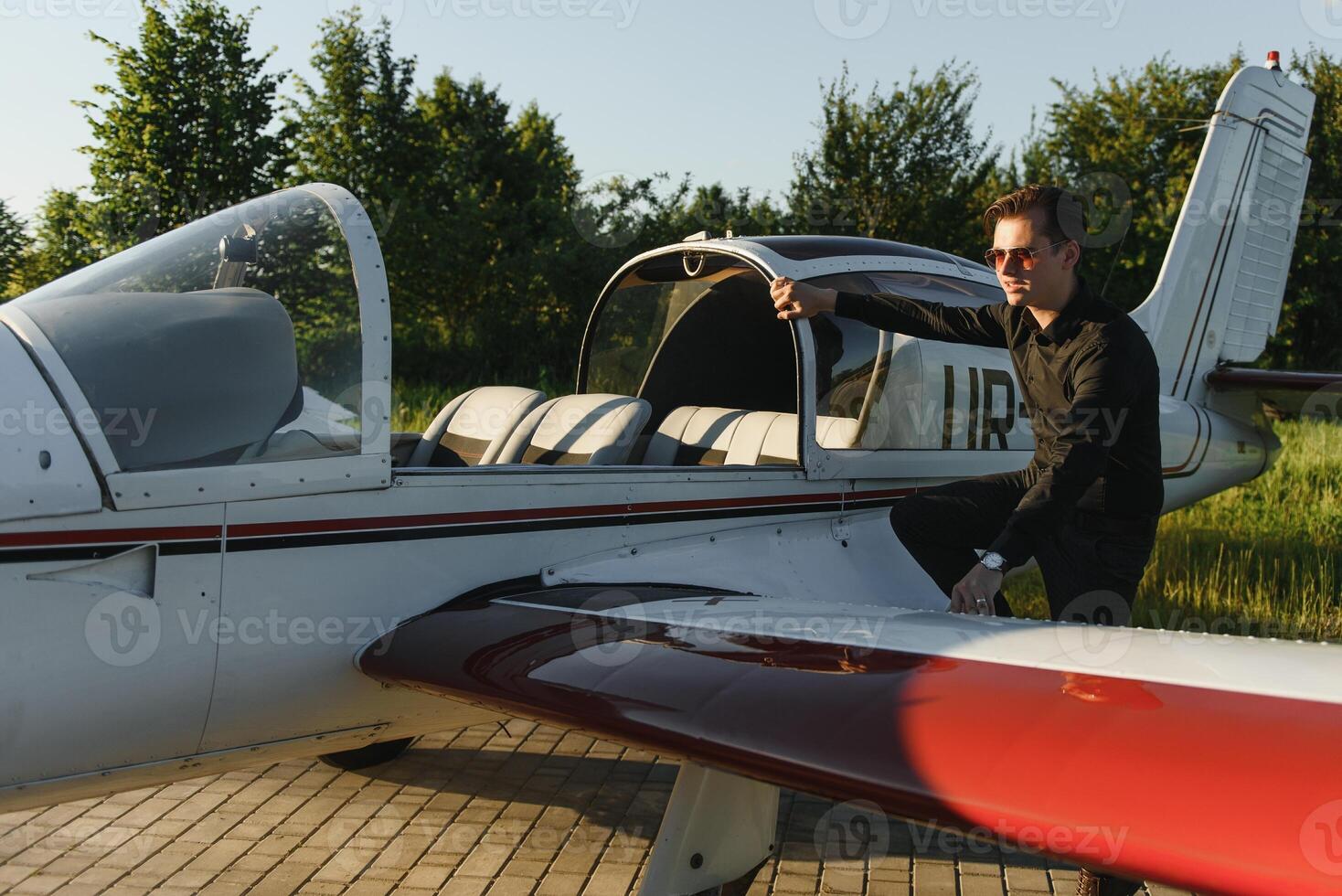 pensativo atraente jovem homem piloto em pé perto pequeno aeronave foto