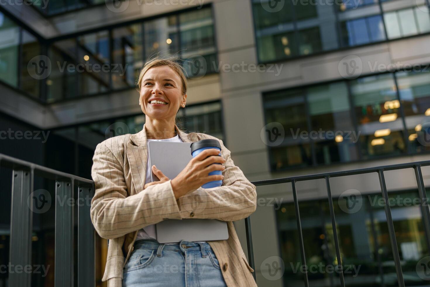 vendas Gerente em pé com computador portátil e café em escritório terraço durante pausa Tempo e parece longe foto