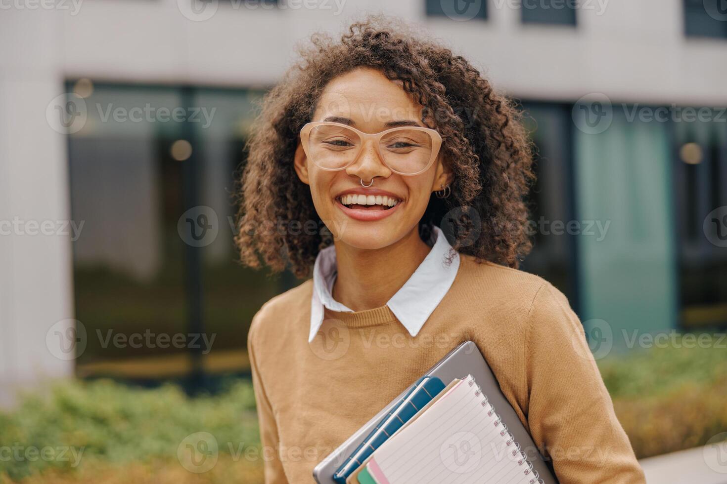 jovem sorridente fêmea aluna em pé com computador portátil e Nota almofadas em moderno construção fundos foto