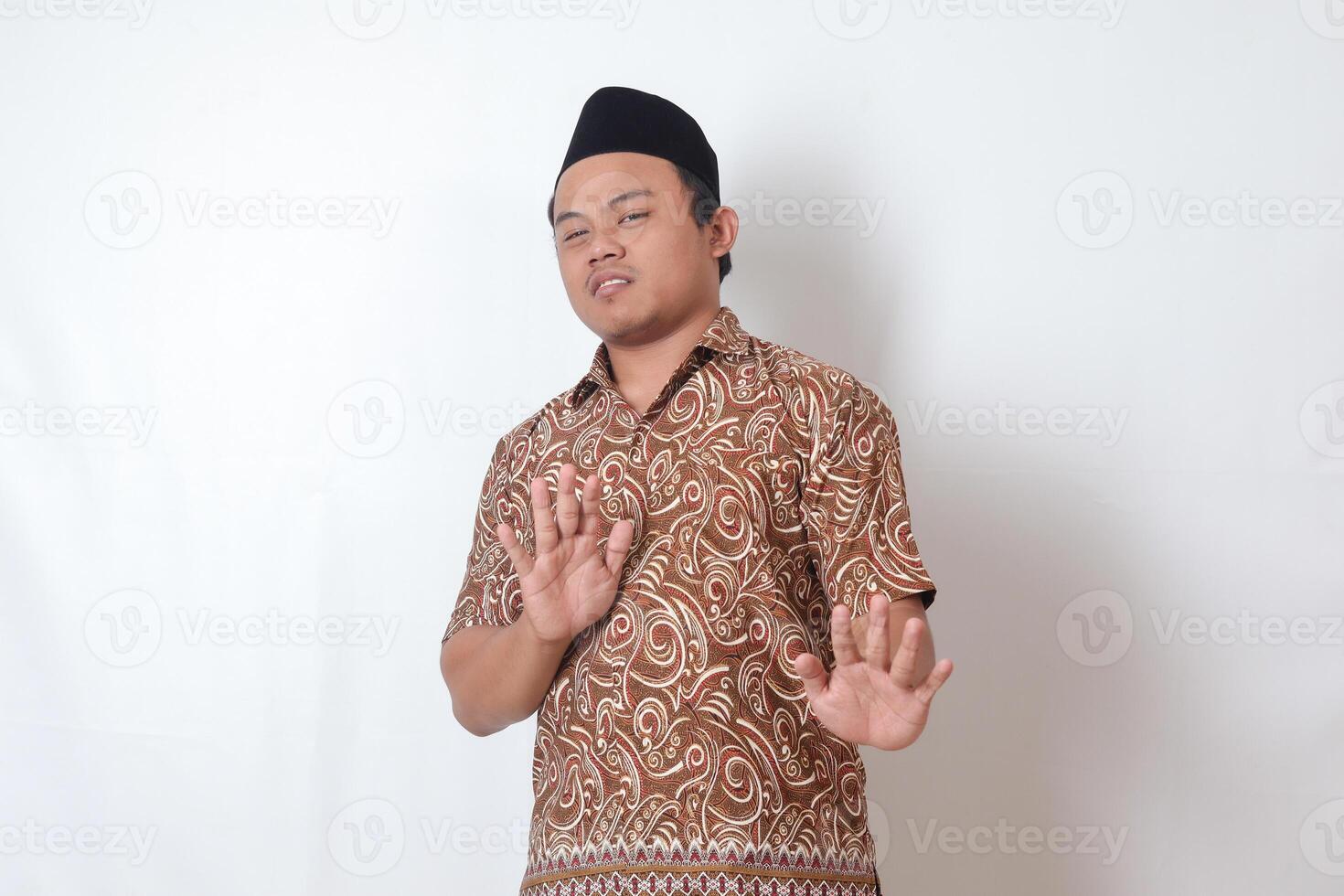 retrato do desagradável ásia homem vestindo batik camisa e Songkok formando uma mão gesto para evitar algo. publicidade conceito. isolado imagem em cinzento fundo foto