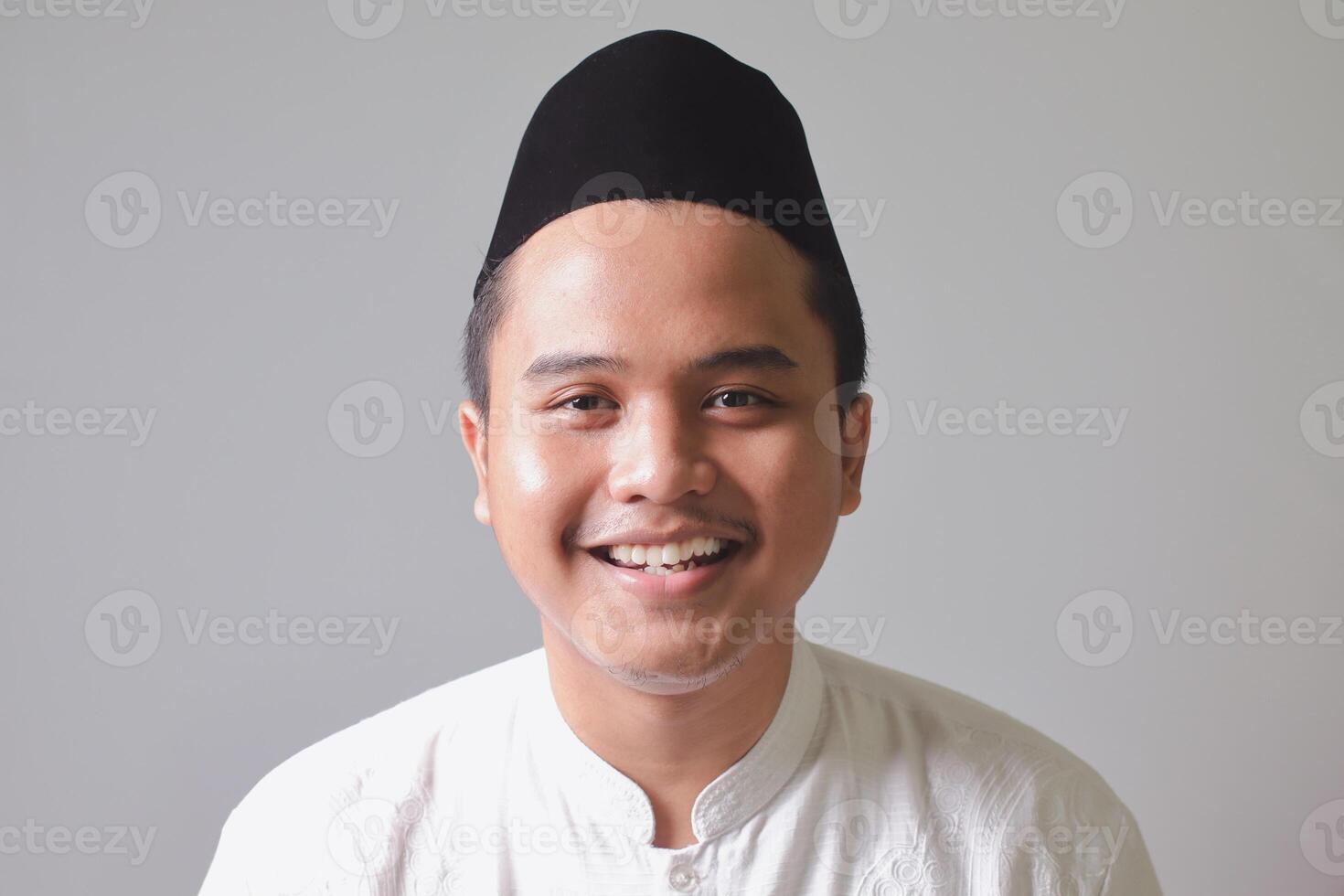 fechar acima retrato do religioso ásia homem dentro Koko camisa ou branco muçulmano camisa e Preto boné, sorridente às Câmera. isolado imagem em cinzento fundo foto