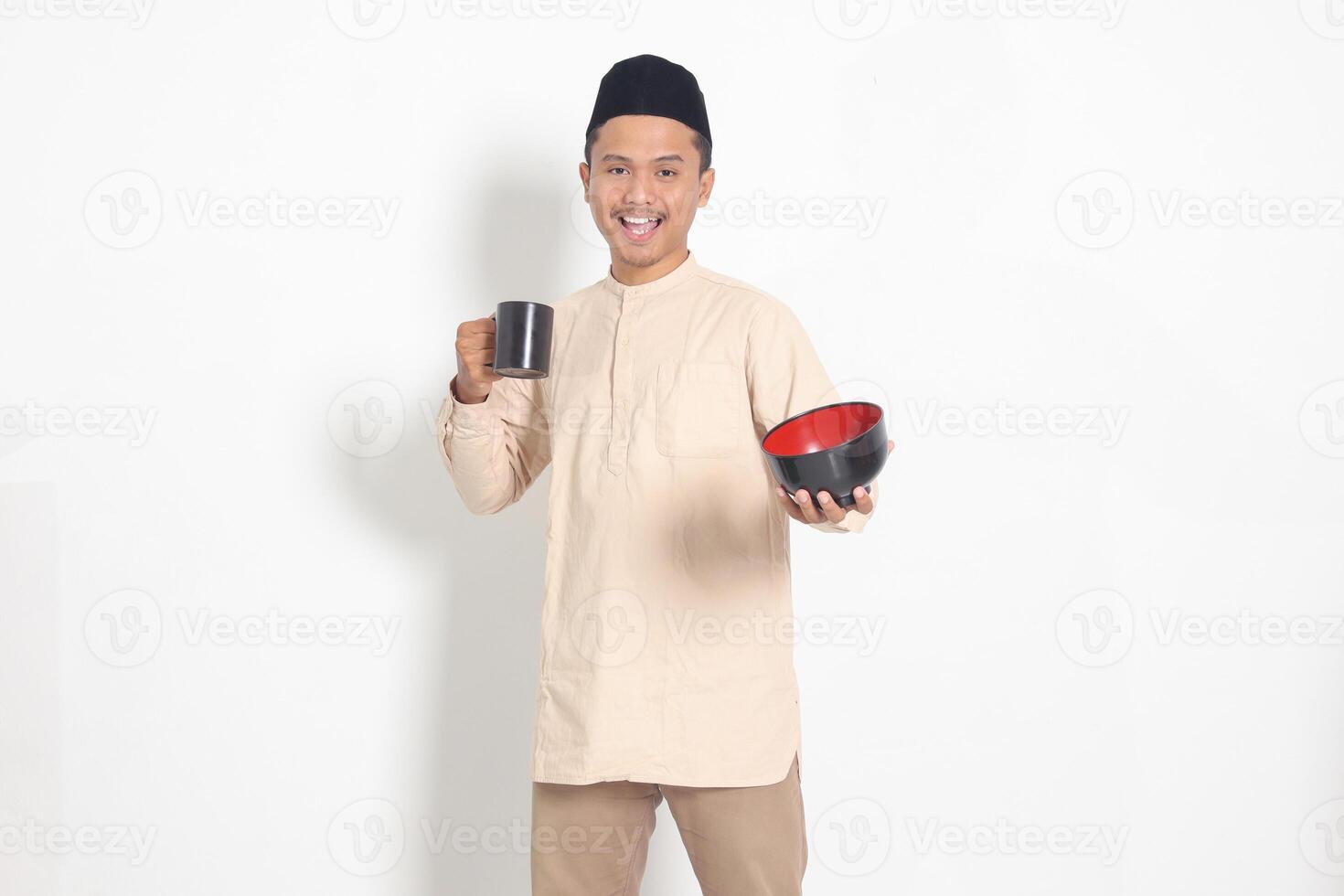 retrato do animado ásia muçulmano homem dentro Koko camisa com calota craniana segurando uma caneca e esvaziar tigela. tigela modelo para Comida marca. isolado imagem em branco fundo foto