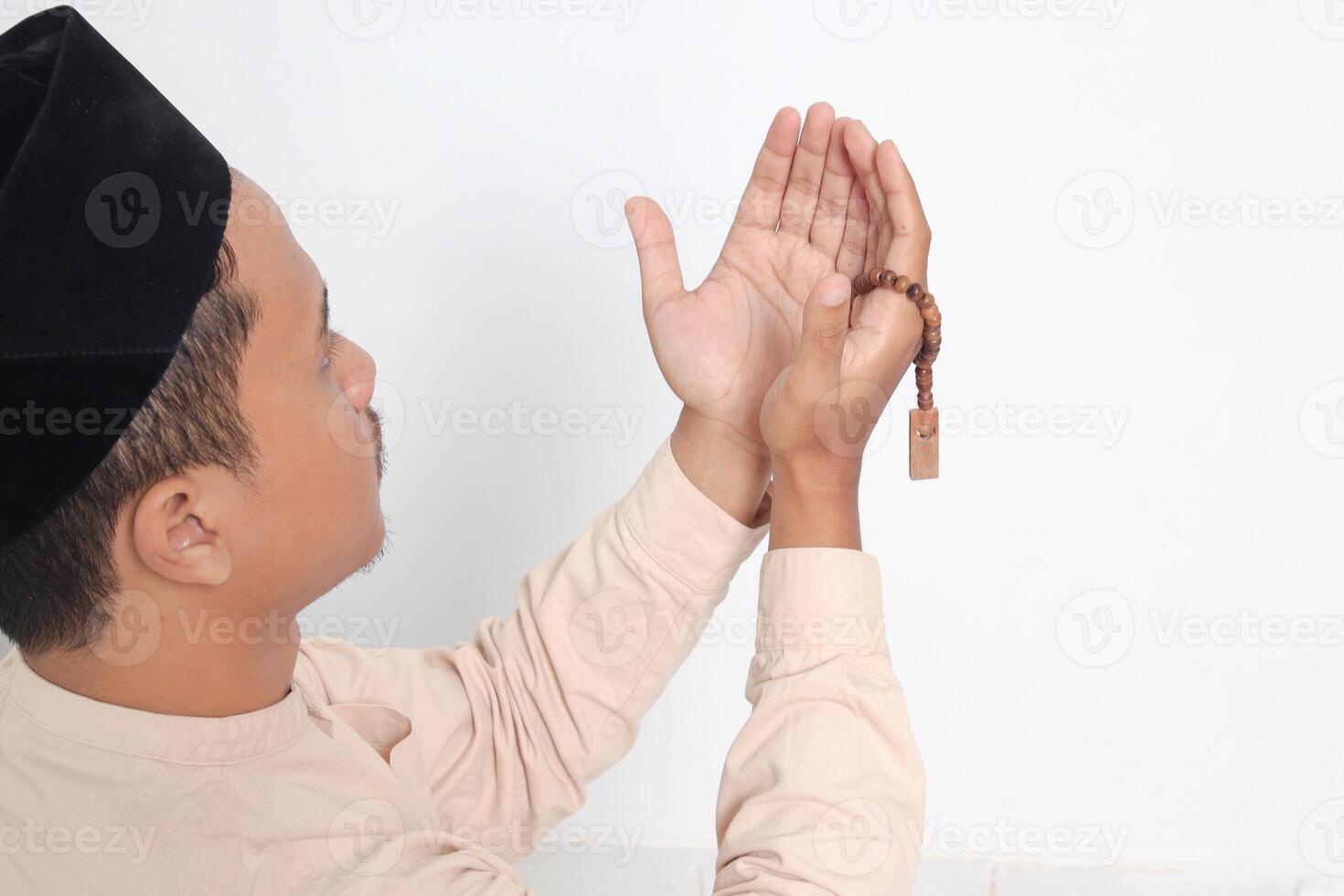 costas Visão retrato do religioso ásia muçulmano homem dentro Koko camisa com calota craniana Rezar sinceramente com dele mãos criado, segurando islâmico miçangas. devoto fé conceito. isolado imagem em branco fundo foto