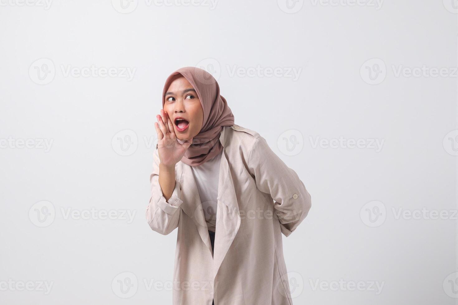 retrato do animado ásia hijab mulher dentro casual terno gritando anúncio e sussurrando fofoca. empresária conceito. isolado imagem em branco fundo foto