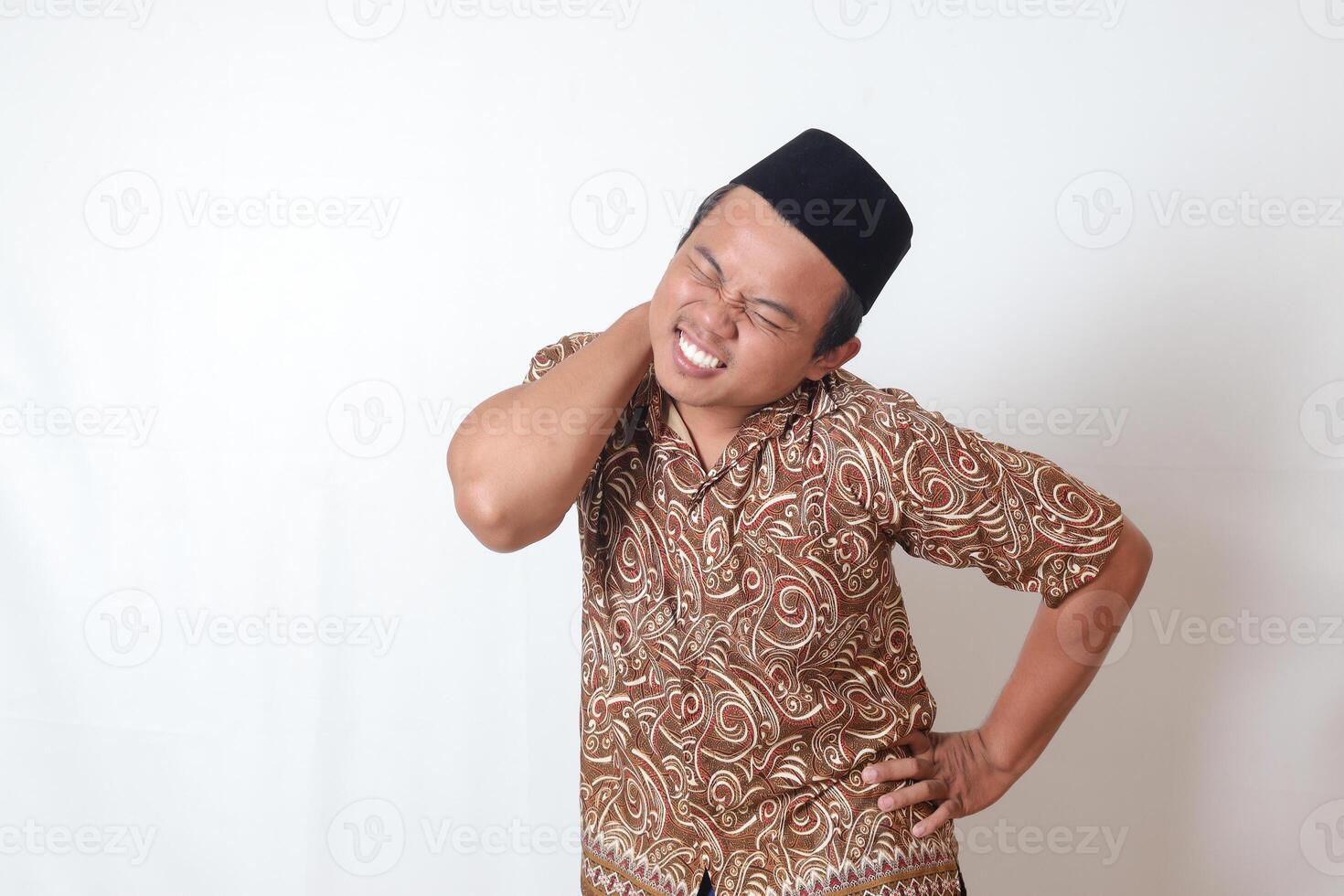 retrato do sofrimento ásia homem vestindo batik camisa e Songkok tendo dor de garganta enquanto tocante dele voltar. isolado imagem em cinzento fundo foto