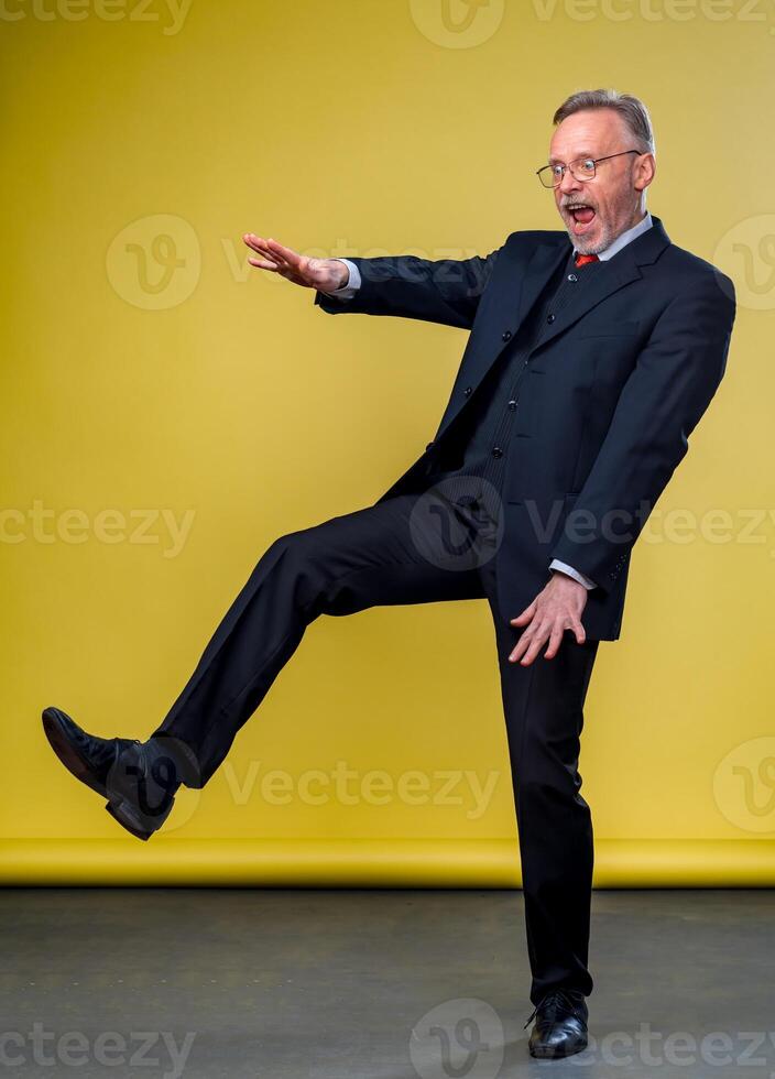 Senior Gerente homem dançando às engraçado pose com expressão. amarelo fundo. foto
