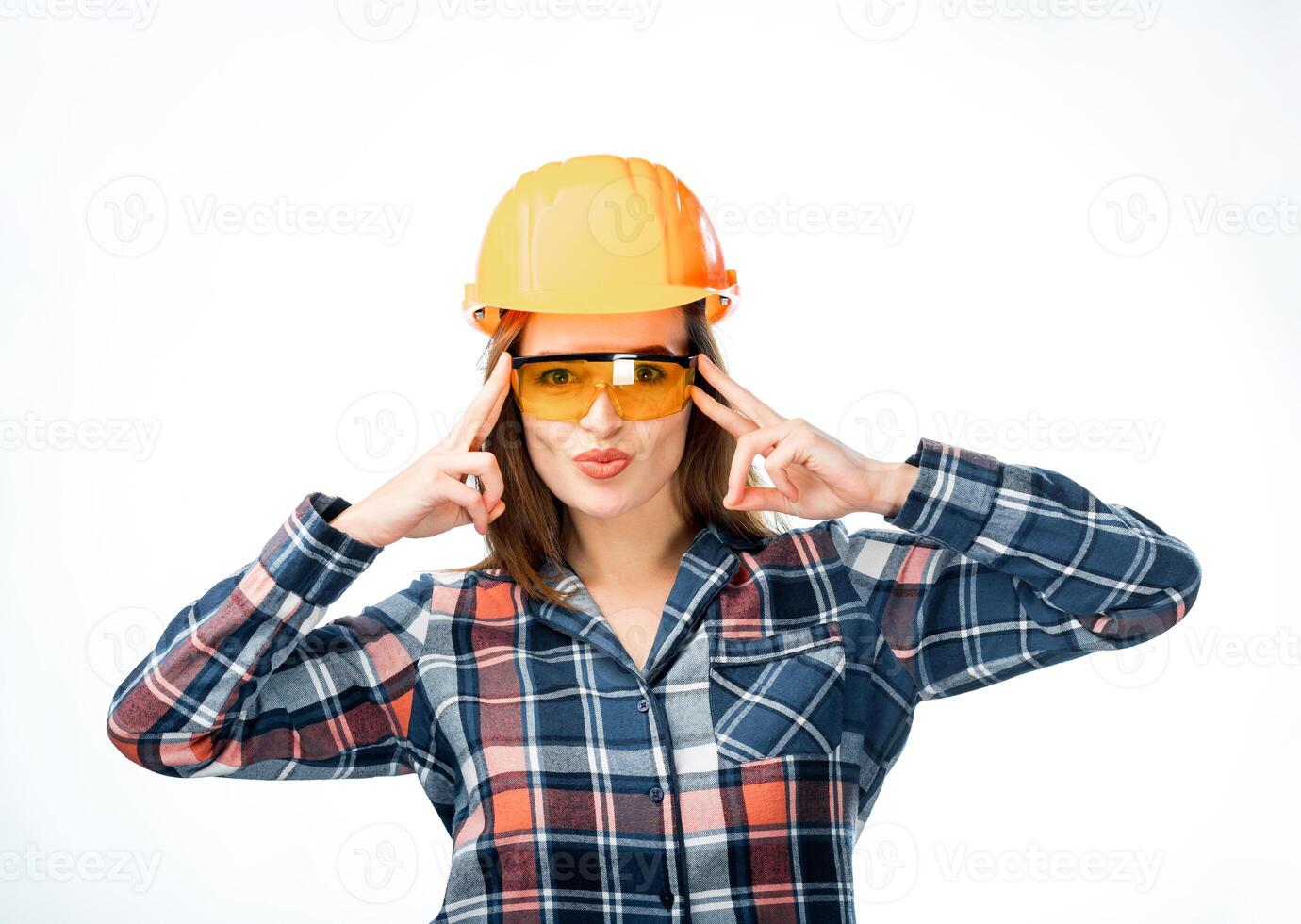 bonita mulher vestindo laranja protetora capacete e óculos. fêmea segurando dedos perto cabeça. isolado em branco fundo. fêmea construtor dentro segurança capacete foto