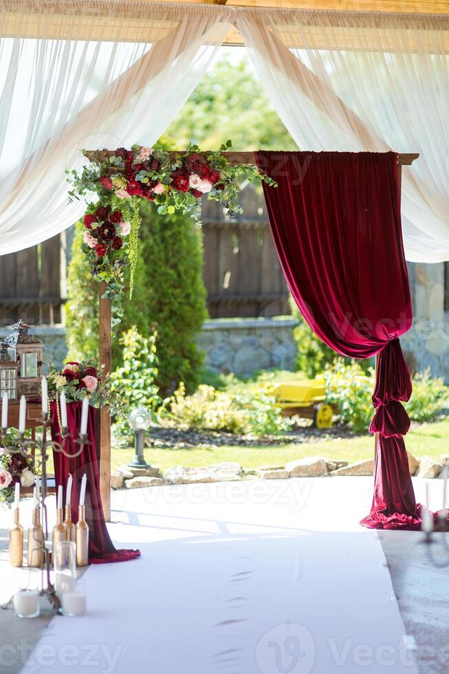 Casamento arco dentro restaurante. Sombrio vermelho flores e Borgonha cortinas. cerimônia decorações. foto