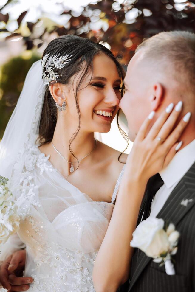 uma jovem noiva e noivo ternamente abraço dentro a raios do a outono Sol. concurso e lindo jovem menina noiva. uma homem Beijos dele amado. contra a fundo do uma lindo jardim foto