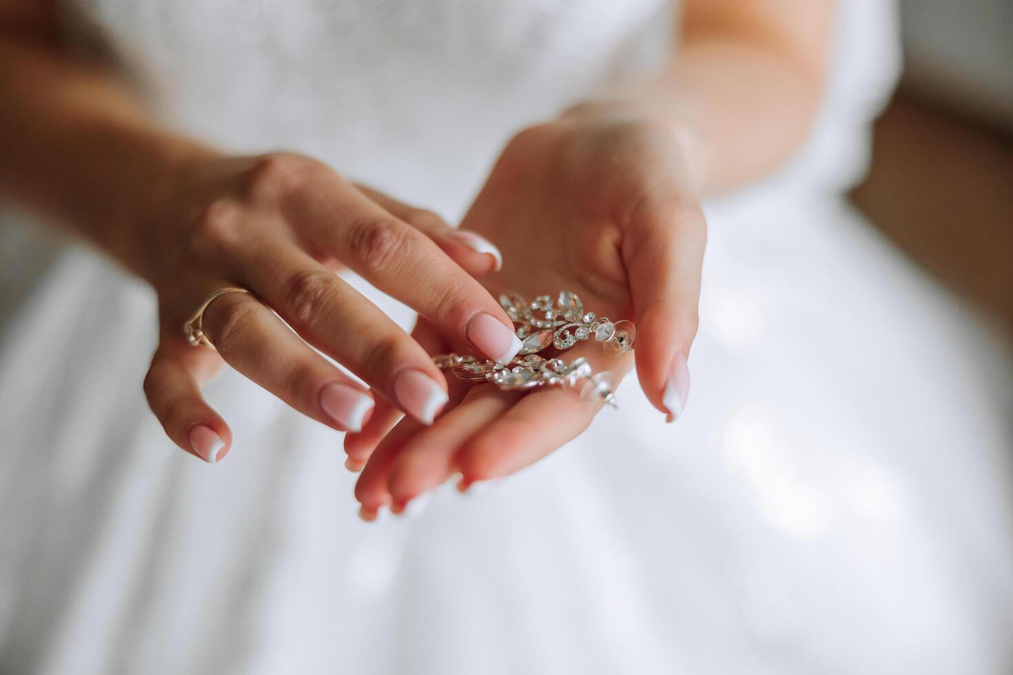 elegante noiva segurando prata brincos. concurso mãos com joia. jovem noiva coloca em dela Casamento decoração foto