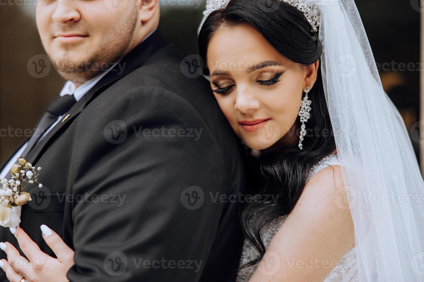 adorável e à moda recém-casados estão abraçando e sorridente contra a fundo do outono natureza dentro uma lindo jardim. a incrivelmente lindo jovem noiva inclinou-se contra a ombro do dela Amado noivo foto