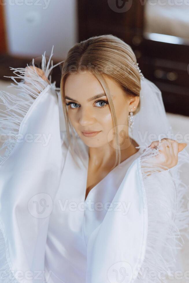 fechar-se loiro noiva com moda Casamento Penteado e inventar. uma jovem noiva com uma sofisticado nupcial penteado dentro de casa de uma janela foto