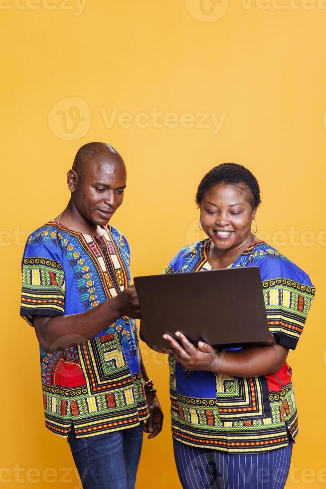 africano americano casal em pé com computador portátil e escolhendo produtos dentro conectados loja. alegre homem e mulher pagando em Internet enquanto compras juntos usando portátil computador foto