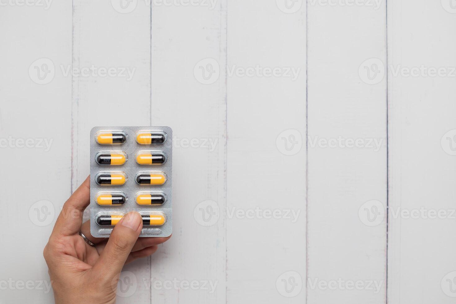 fechar acima do fêmea mão segurando bolha pacote do pílulas em branco de madeira fundo foto