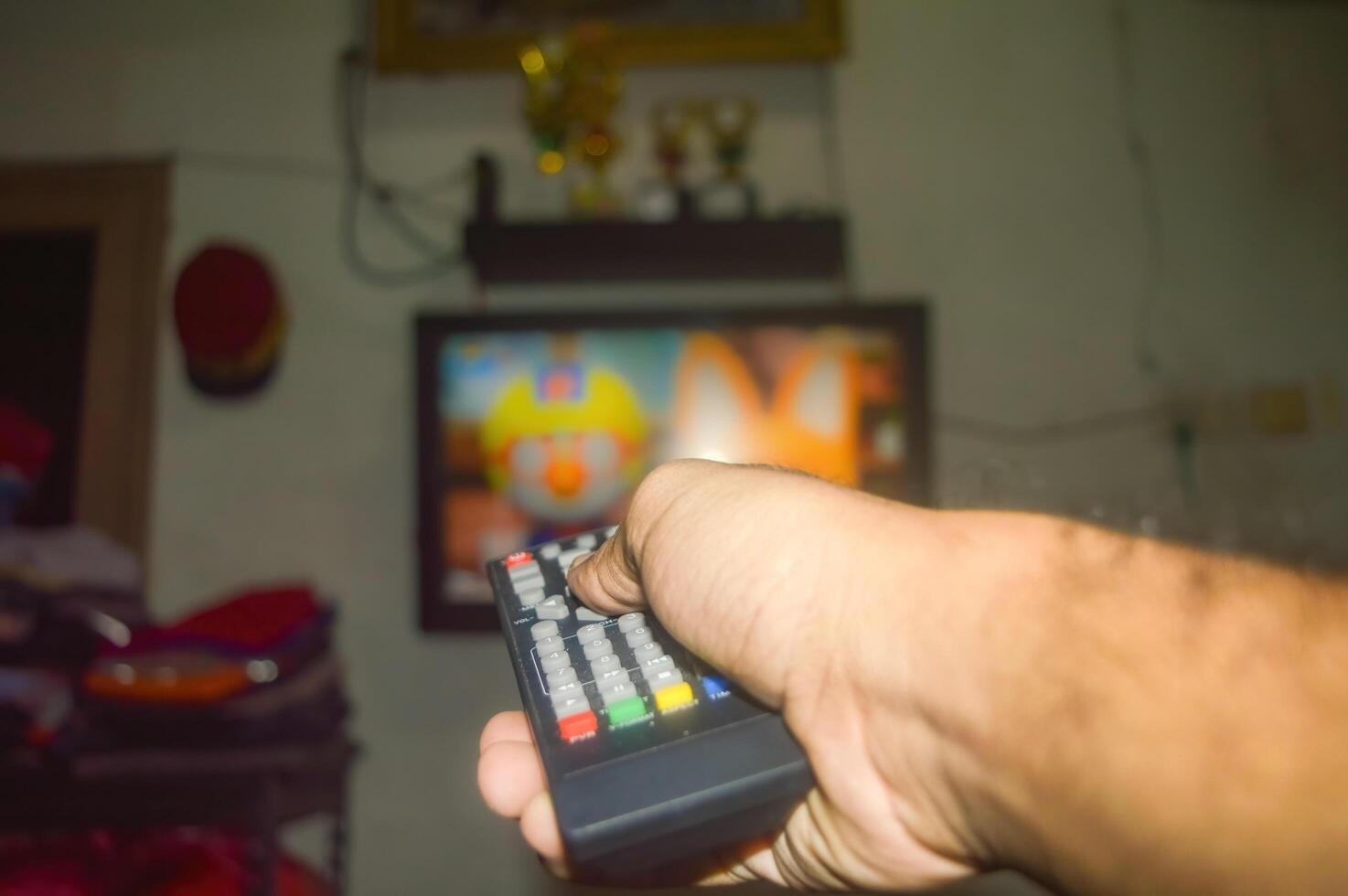 a mão é segurando a televisão controlo remoto dentro frente do uma televisão, preparando para mudança a televisão canal foto