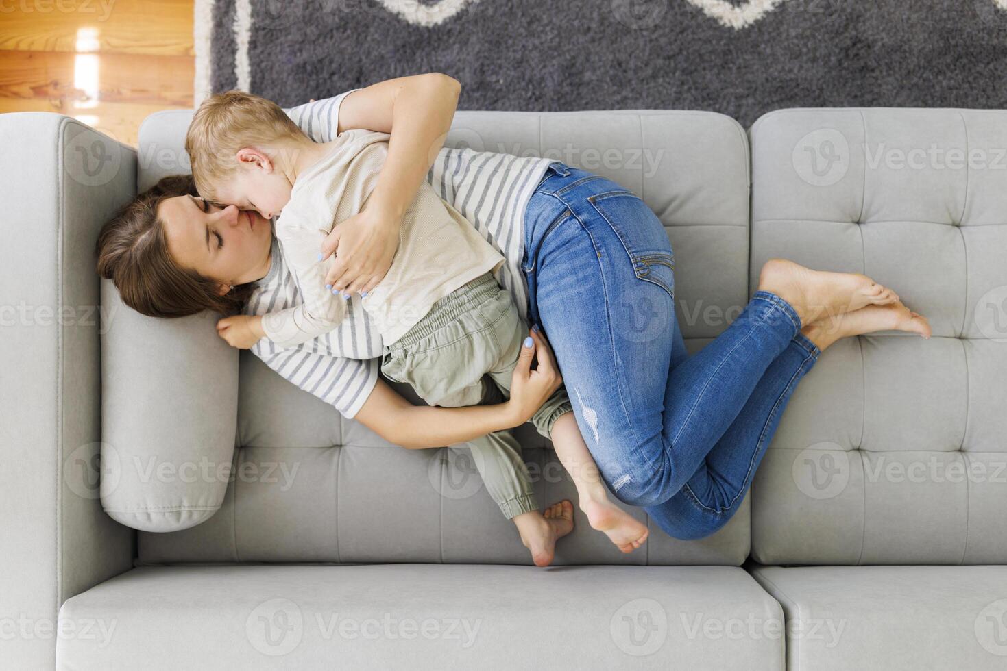 mãe e criança abraço em uma cinzento sofá. interior casual estilo de vida retrato foto