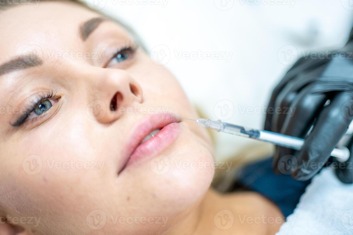 fechar-se do mulher face e mão dentro cirúrgico luva segurando seringa perto dela lábios, pronto para receber beleza tratamento. injeção cosmetologia, lábios aumento e correção conceito. foto