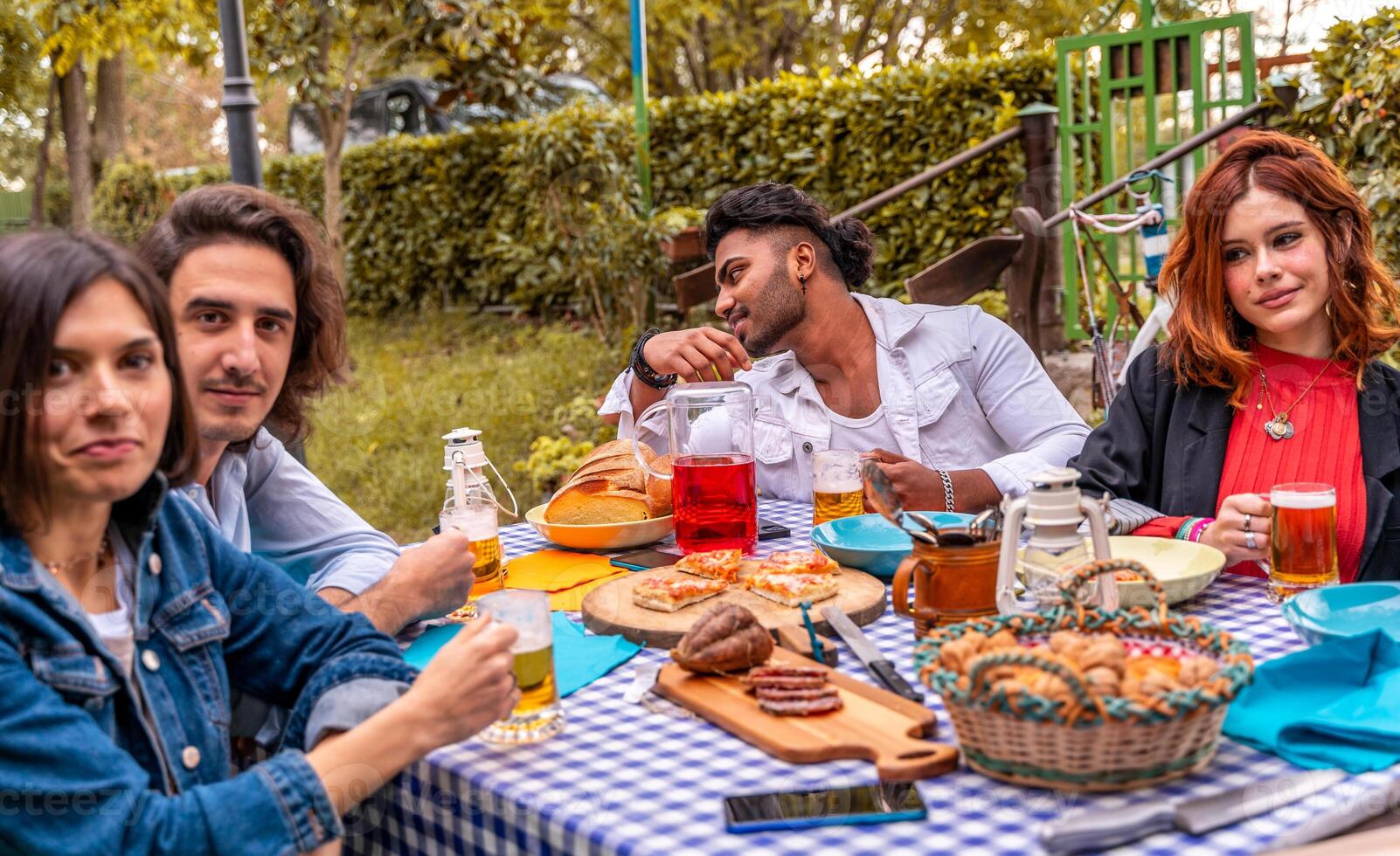 grupo do multicultural amigos tendo Diversão às jardim festa - jovem pessoas sorridente juntos comendo Comida e bebendo Cerveja foto