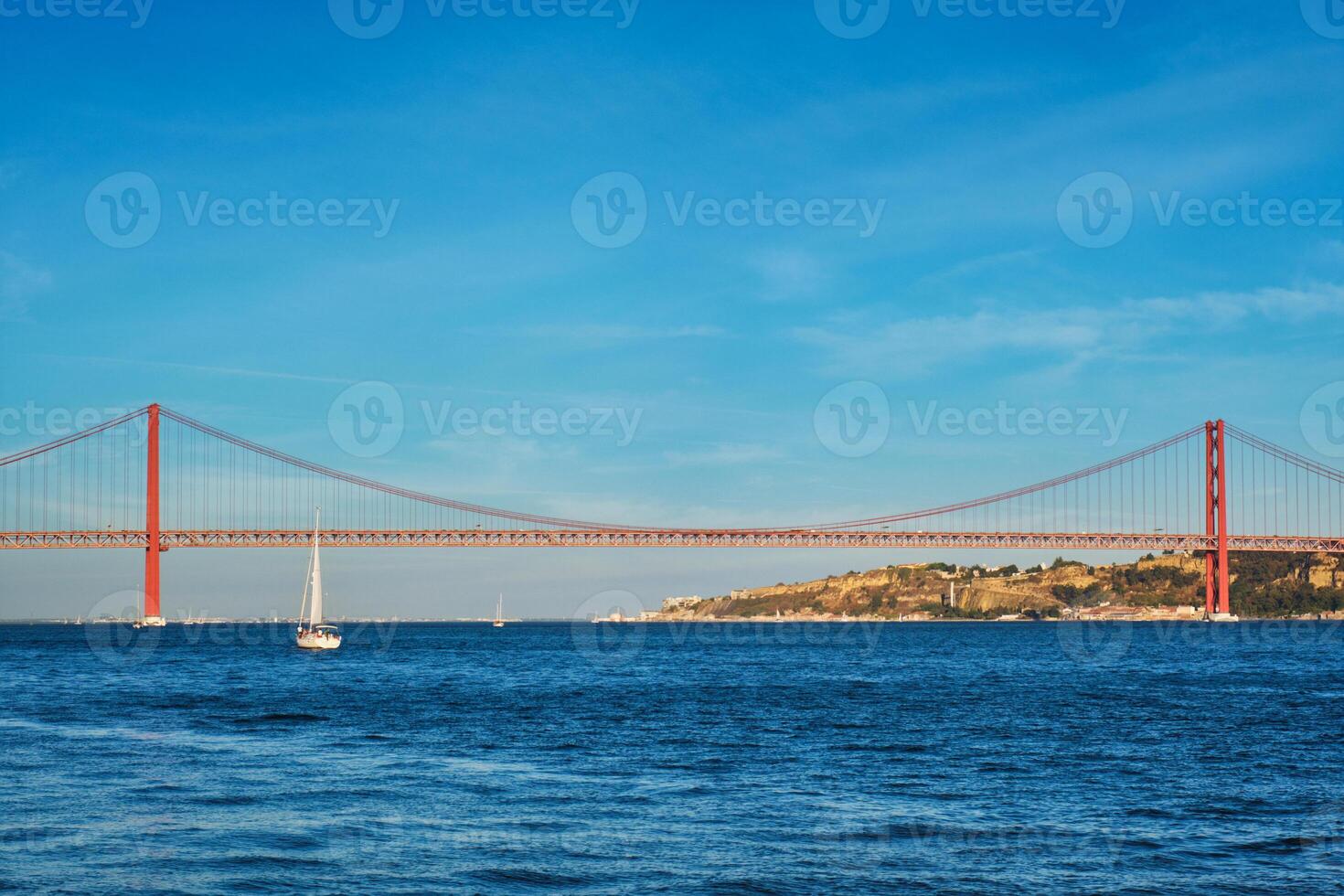 Visão do 25 de abril ponte sobre tagus rio, Cristo a rei monumento e uma iate barco às pôr do sol. Lisboa, Portugal foto