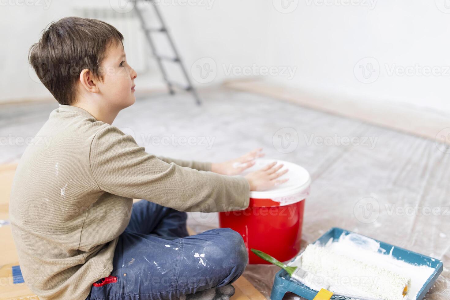 criança tem Diversão sentado em a chão e batendo dele mãos em uma balde do pintura foto