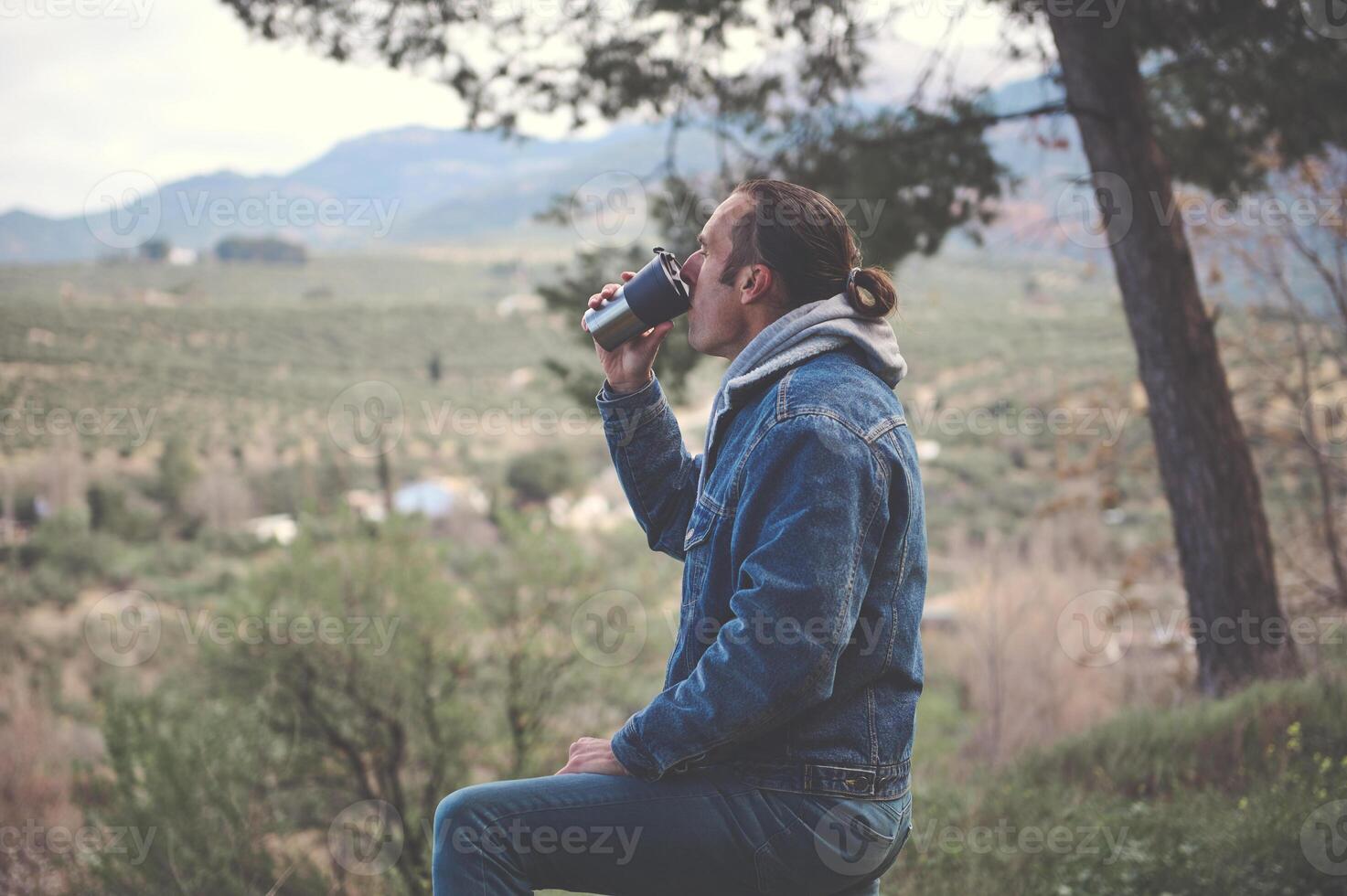 relaxado jovem homem bebendo quente chá ou café a partir de uma garrafa térmica caneca dentro a cedo Primavera floresta. foto