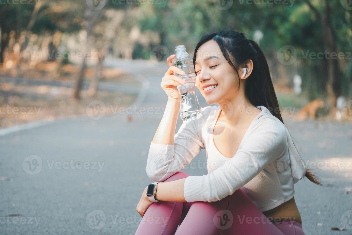 esporte ginástica conceito, uma alegre jovem mulher sentado em uma floresta estrada leva uma água pausa depois de uma correr, desfrutando dela ginástica rotina ao ar livre. foto