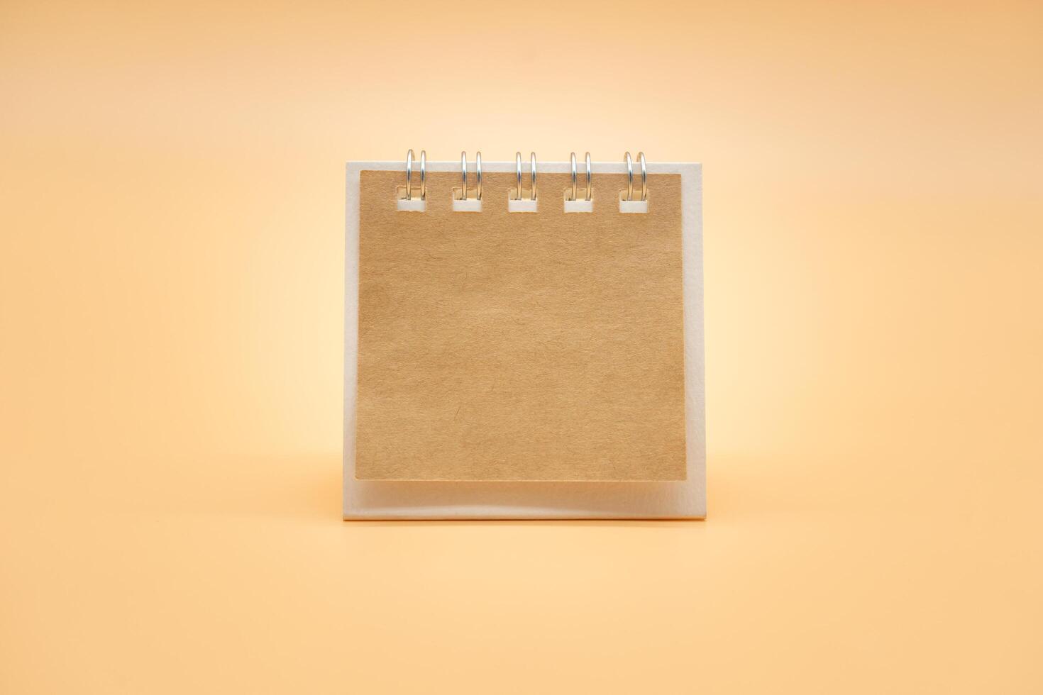 em branco calendário com Castanho papel isolado em laranja fundo. em branco papel escrivaninha espiral calendário. fechar acima do uma em branco reciclar papel modelo. foto