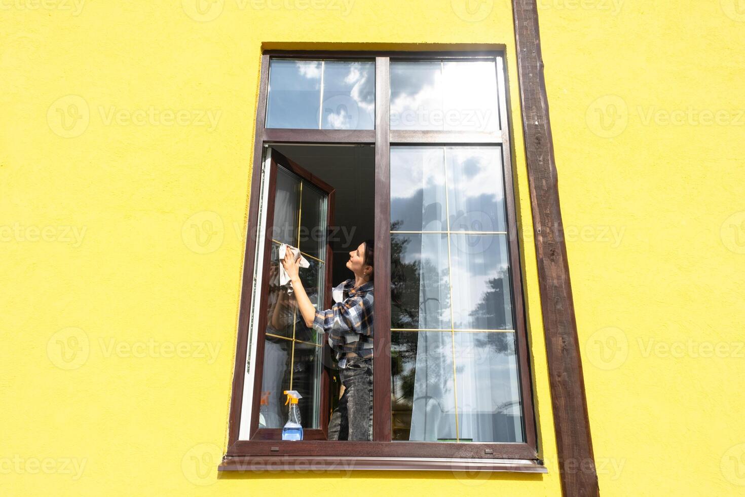 uma mulher manualmente lavagens a janela do a casa com uma trapo com uma spray limpador e uma esfregão fora. segurança às altura, restaurando ordem e limpeza dentro a primavera, limpeza serviço foto