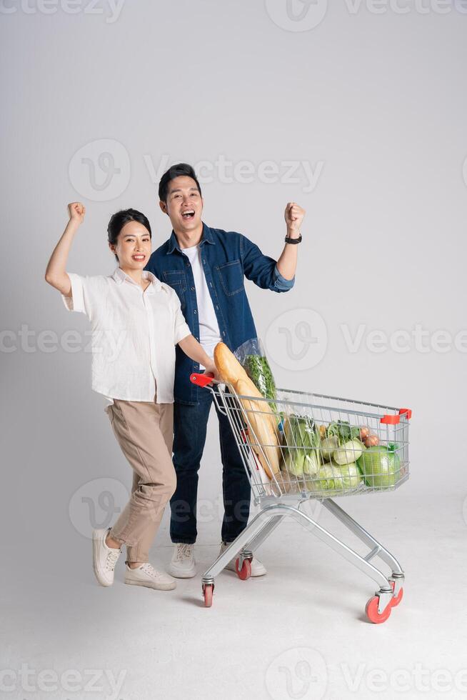 imagem do ásia casal empurrando supermercado carrinho enquanto compras, isolado em branco fundo foto