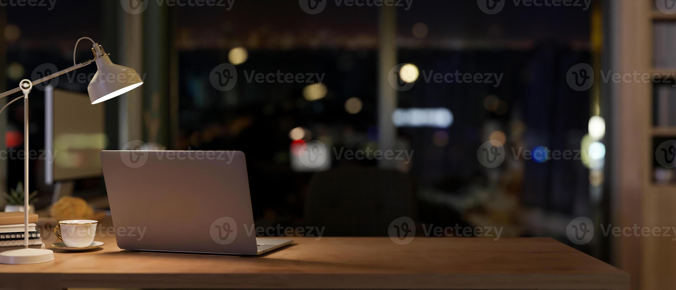 uma computador portátil dentro uma contemporâneo escritório quarto às noite iluminado de escuro luzes a partir de uma mesa lâmpada. foto