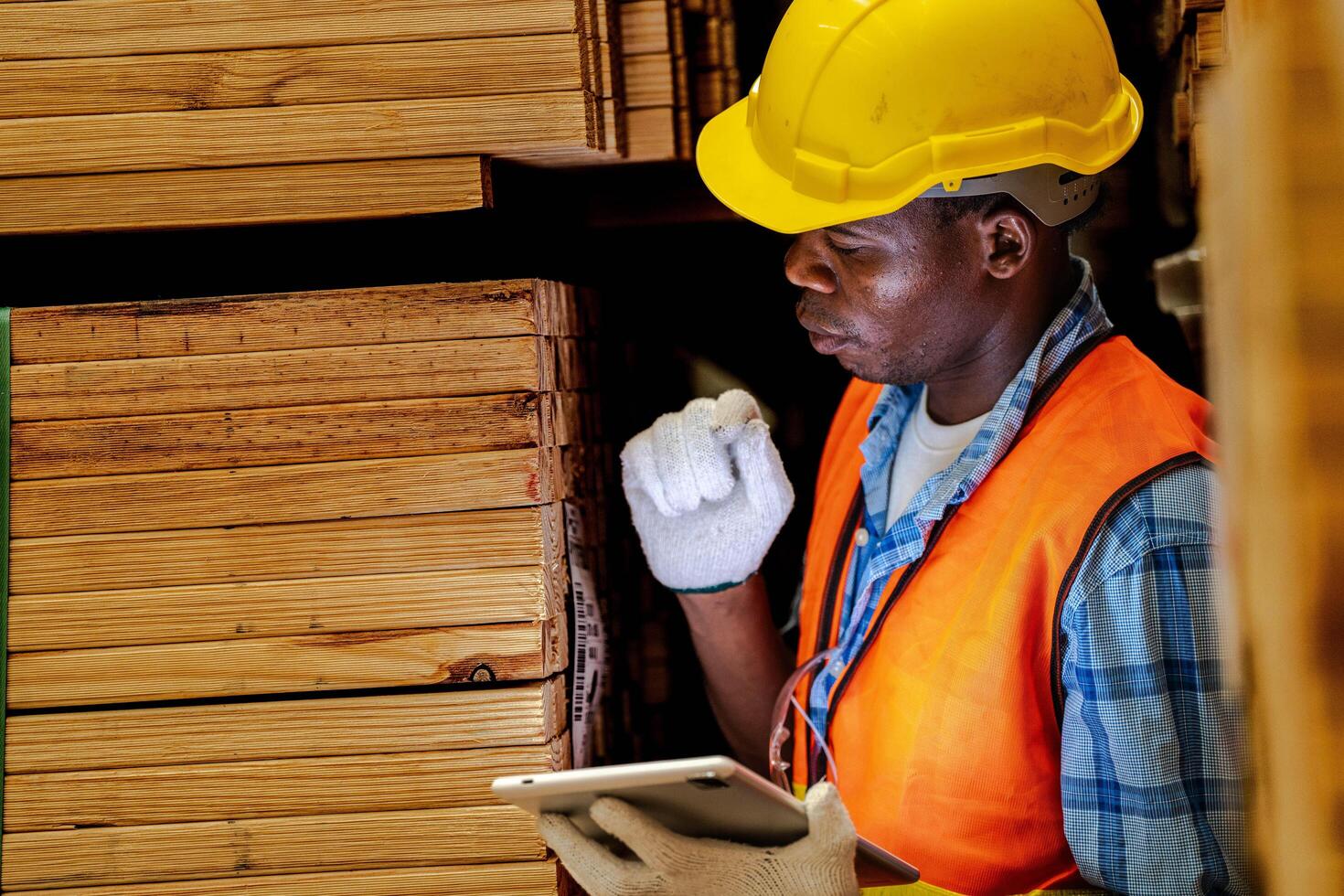 africano trabalhador carpinteiro vestindo segurança uniforme e Difícil chapéu trabalhando e verificação a qualidade do de madeira produtos às oficina fabricação. homem e mulher trabalhadores madeira dentro Sombrio armazém indústria. foto