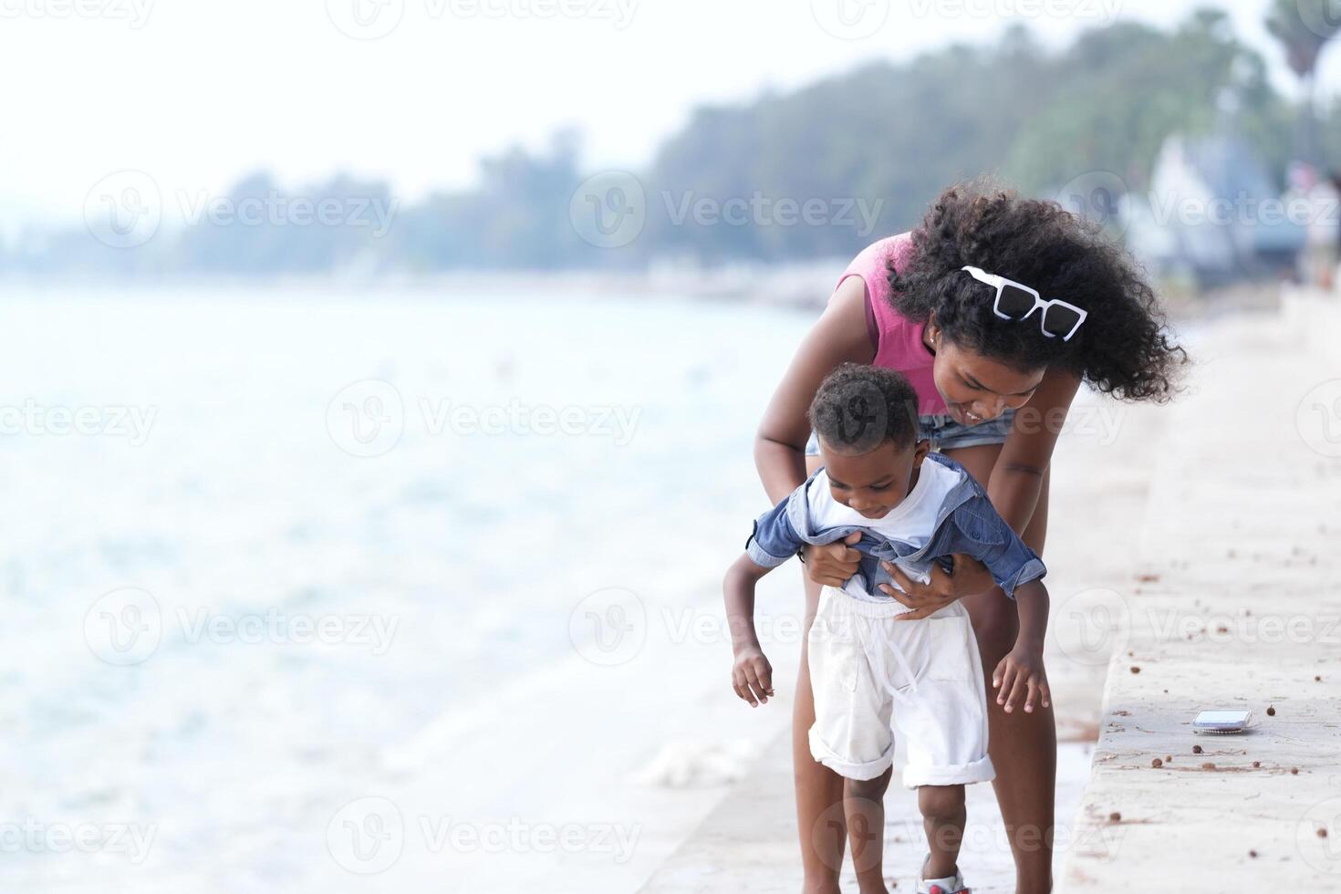 misturado raça africano e ásia mãe e Garoto é jogando às a ao ar livre área. sorridente feliz família ter Diversão corrida em a de praia. retrato do mãe e criança estilo de vida com uma único Penteado. foto