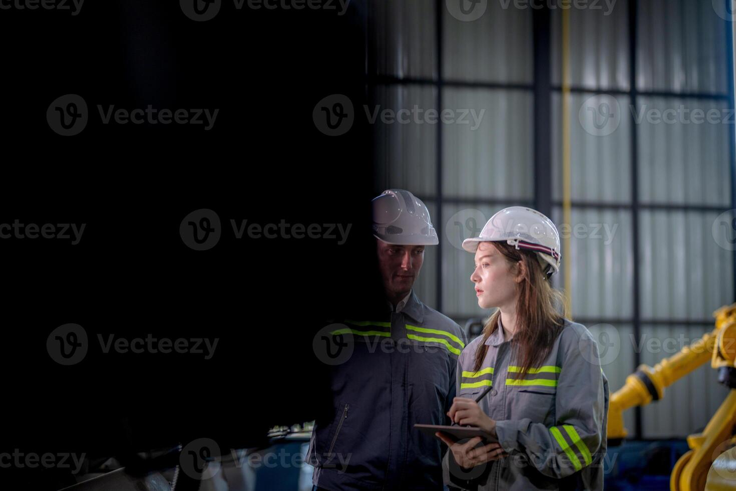 fábrica engenheiro mulher inspecionando em máquina com inteligente tábua. trabalhador trabalho às máquina robô braço. a Soldagem máquina com uma controlo remoto sistema dentro a industrial fábrica. artificial inteligência conceito. foto