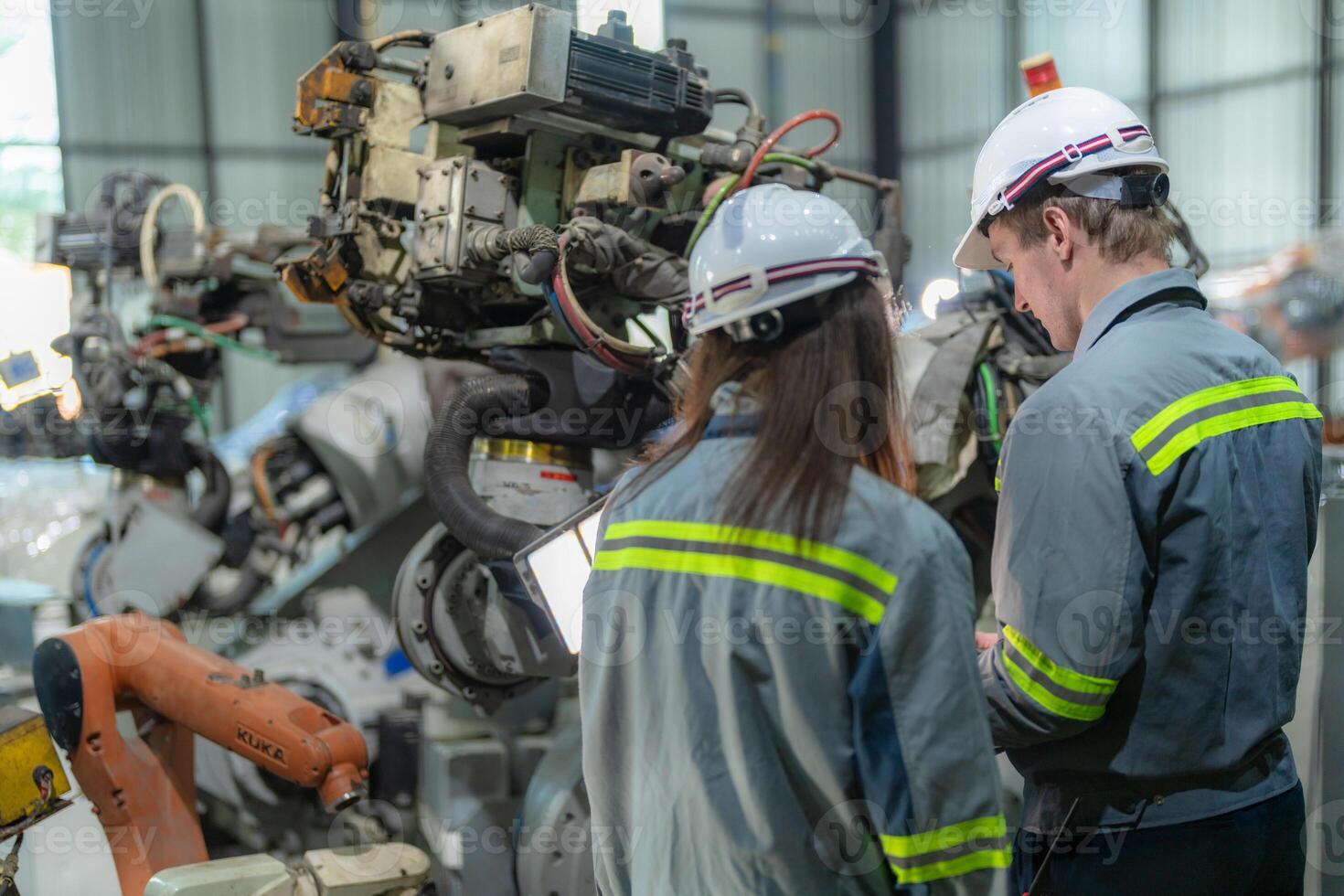 fábrica engenheiro mulher inspecionando em máquina com inteligente tábua. trabalhador trabalho às máquina robô braço. a Soldagem máquina com uma controlo remoto sistema dentro a industrial fábrica. artificial inteligência conceito. foto