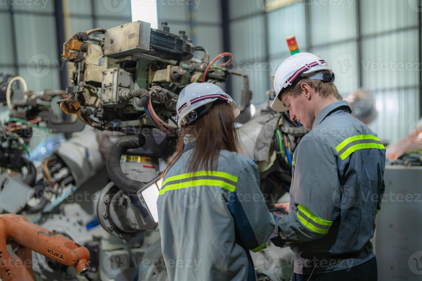 fábrica engenheiro mulher inspecionando em máquina com inteligente tábua. trabalhador trabalho às máquina robô braço. a Soldagem máquina com uma controlo remoto sistema dentro a industrial fábrica. artificial inteligência conceito. foto