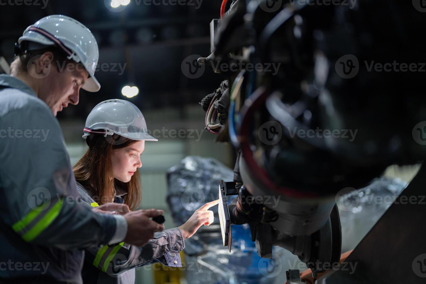 fábrica engenheiro mulher inspecionando em máquina com inteligente tábua. trabalhador trabalho às máquina robô braço. a Soldagem máquina com uma controlo remoto sistema dentro a industrial fábrica. artificial inteligência conceito. foto