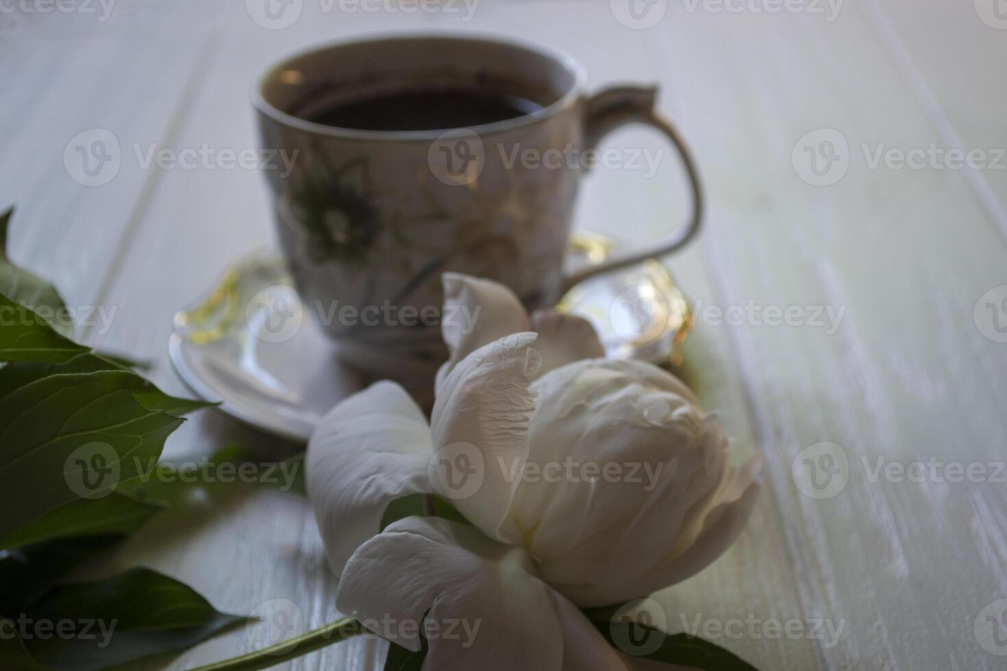 uma copo do café e branco peônia em uma branco mesa. foto