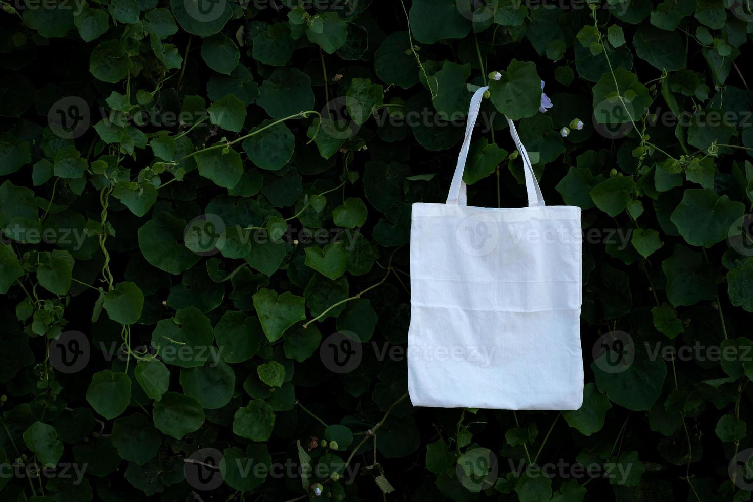 Saco de pano branco em branco com fundo de folhagem de árvores de arbusto verde foto