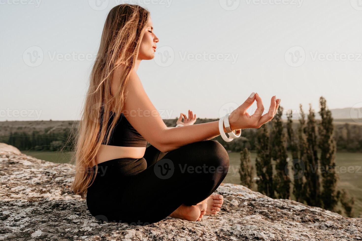 ginástica mulher. bem olhando meio envelhecido mulher com grandes cabelo, ginástica instrutor dentro perneiras e tops fazendo alongamento e pilates em a Rocha perto floresta. fêmea ginástica ioga rotina conceito. foto