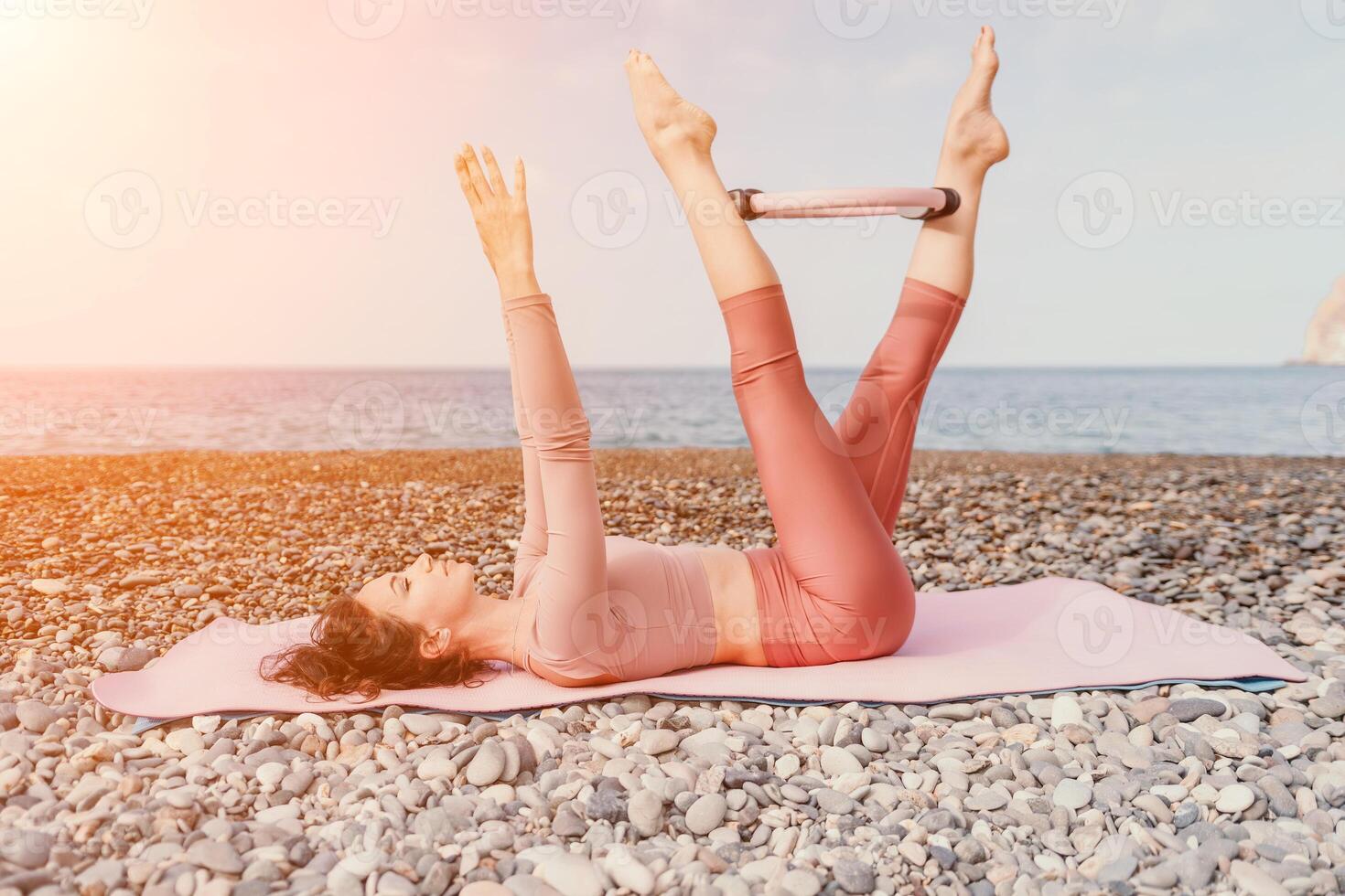 mulher mar pilates. desportivo feliz meio envelhecido mulher praticando ginástica em de praia perto mar, sorridente ativo fêmea Treinamento com anel em ioga esteira fora, desfrutando saudável estilo de vida, harmonia e meditação foto