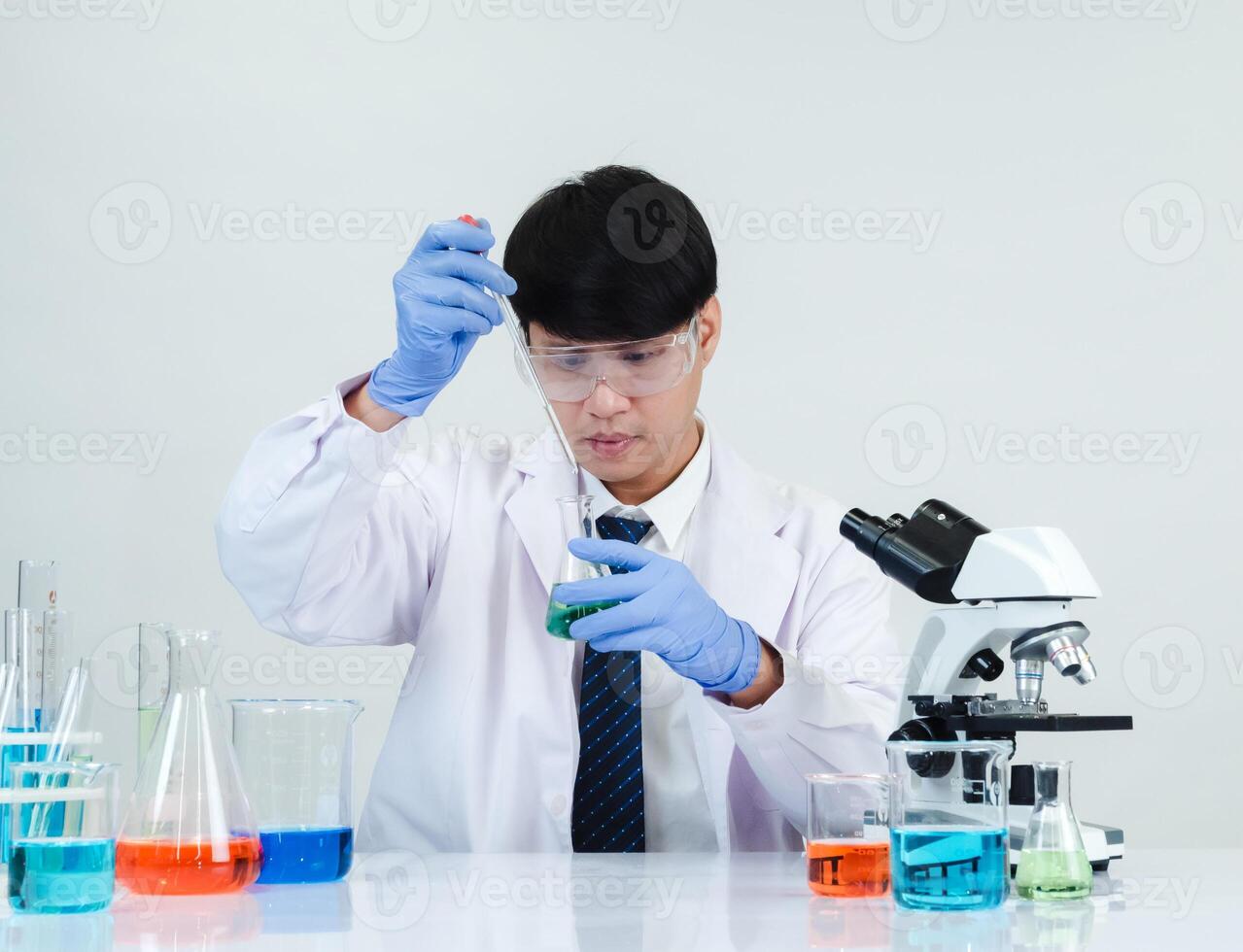 retrato ásia homem aluna cientista médico vestido 1 pessoa sti dentro laboratório olhando mão segurando teste tubo químico. causou de mistura reagentes dentro científico pesquisa laboratórios e microscópio em mesa foto