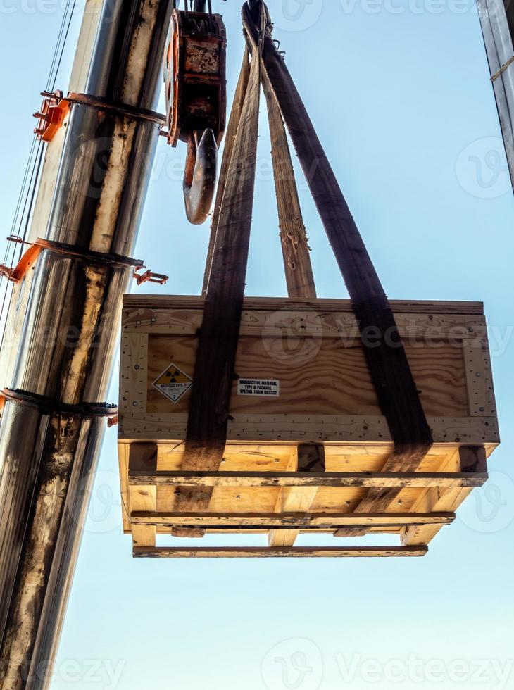 o guindaste levantando o suporte do instrumento radioativo para transporte da caixa de madeira foto