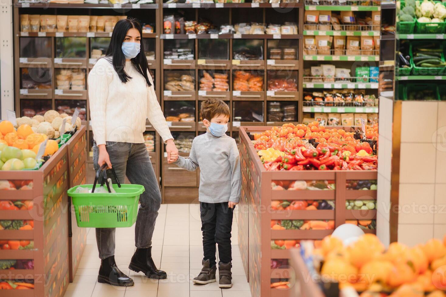 jovem mulher e dela criança vestindo protetora face máscaras fazer compras uma Comida às uma supermercado durante a coronavírus epidemia ou gripe surto. foto