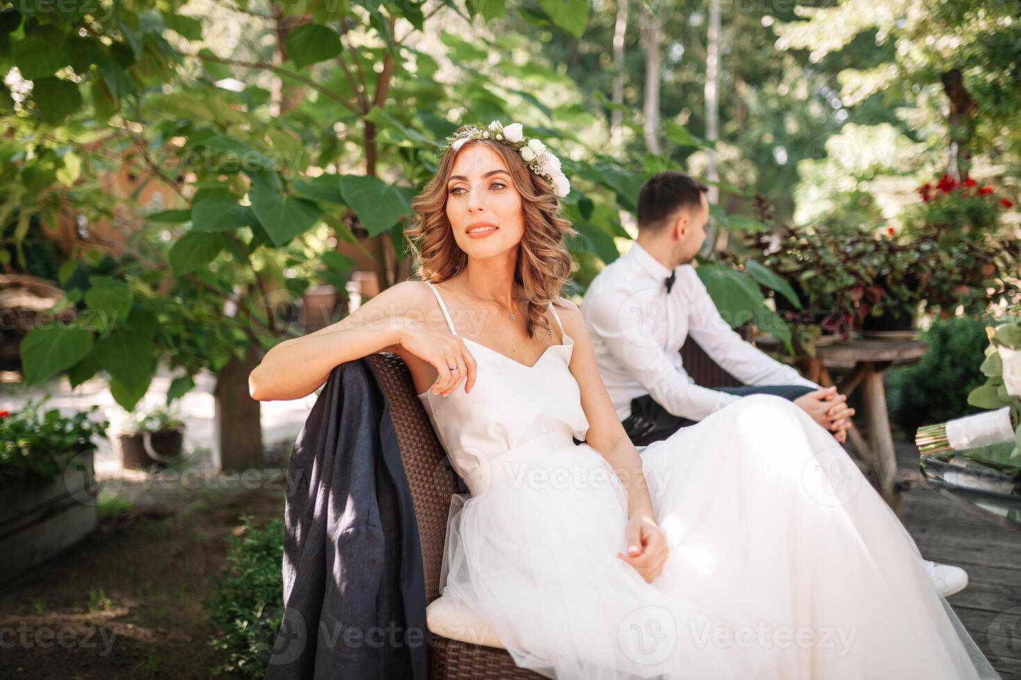 uma lindo noiva dentro uma branco Casamento vestir e guirlanda senta em uma cadeira Próximo para a noivo, em repouso e preparando para uma feliz família vida foto