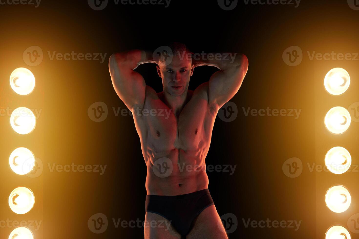 ativo estilo de vida conceito. profissional fisiculturista mostrando perfeito muscular corpo, lâmpadas iluminação em fundo foto