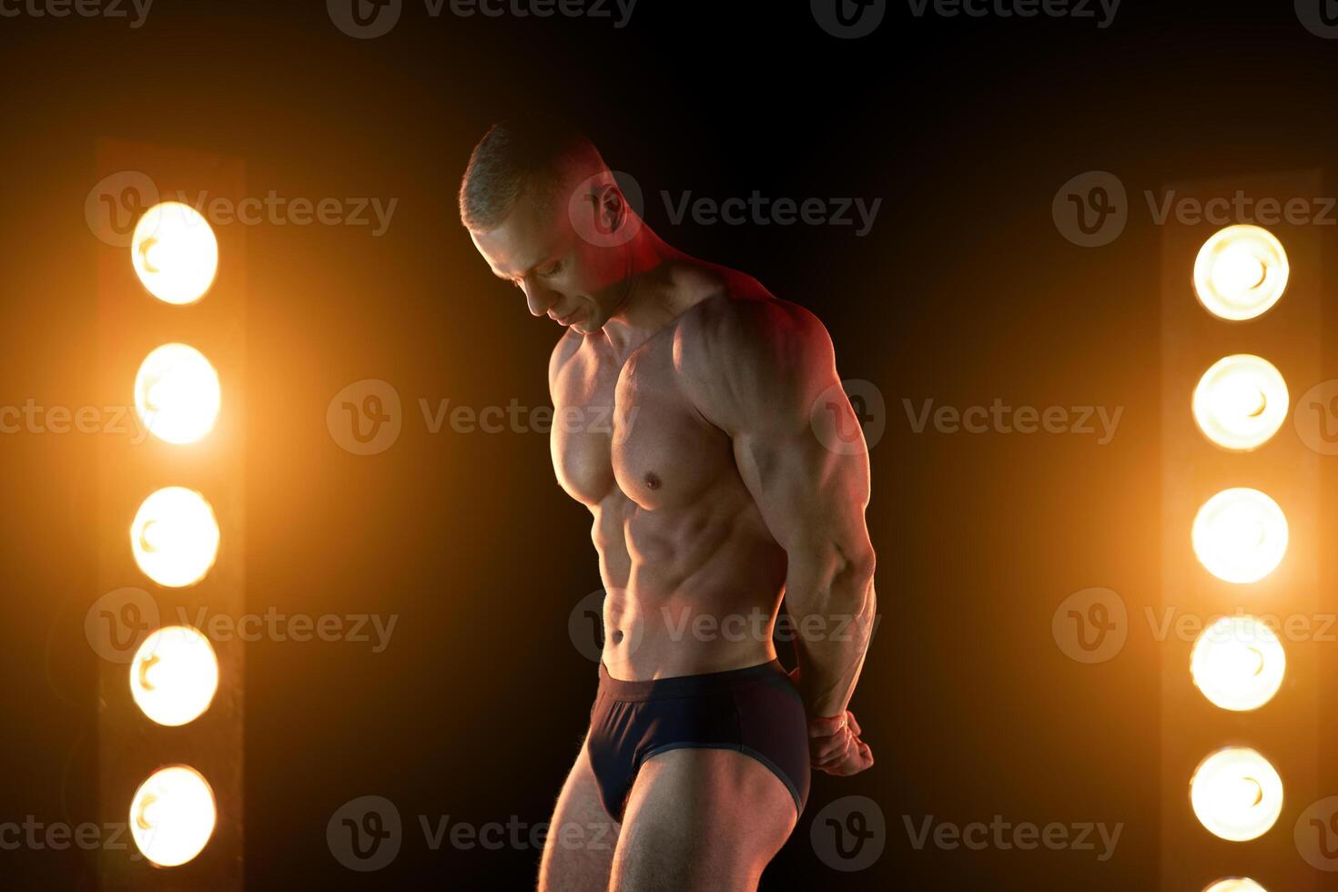 ativo estilo de vida conceito. profissional fisiculturista mostrando perfeito muscular corpo, lâmpadas iluminação em fundo foto