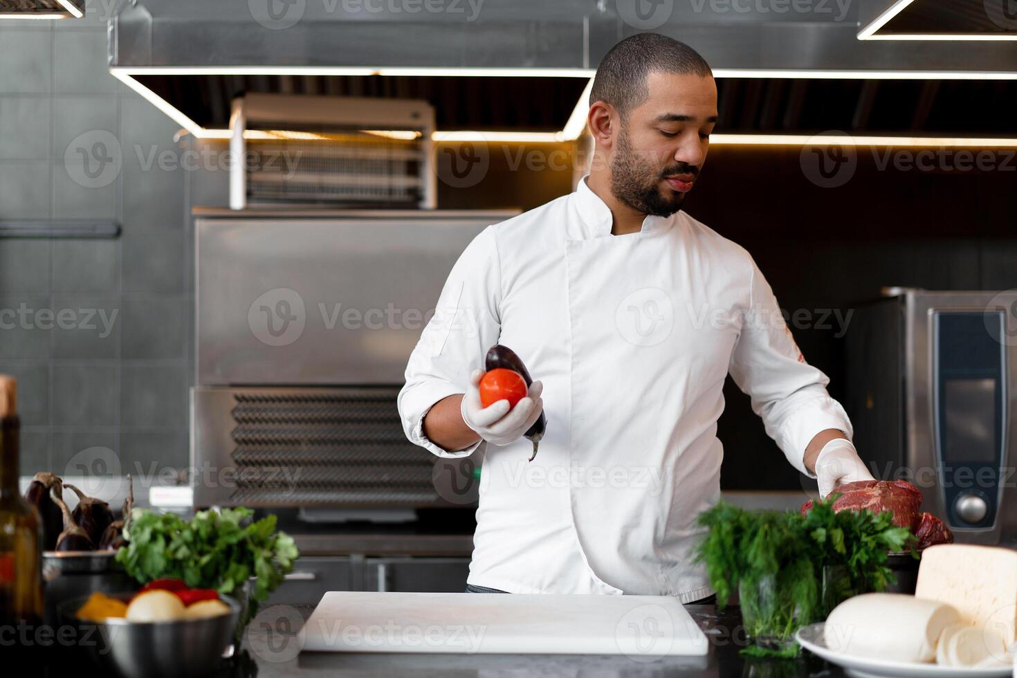 feliz sorridente chefe de cozinha prepara carne prato com vários legumes dentro a cozinha. dentro 1 mão a homem detém vegetais, dentro a de outros uma peça do fresco carne foto