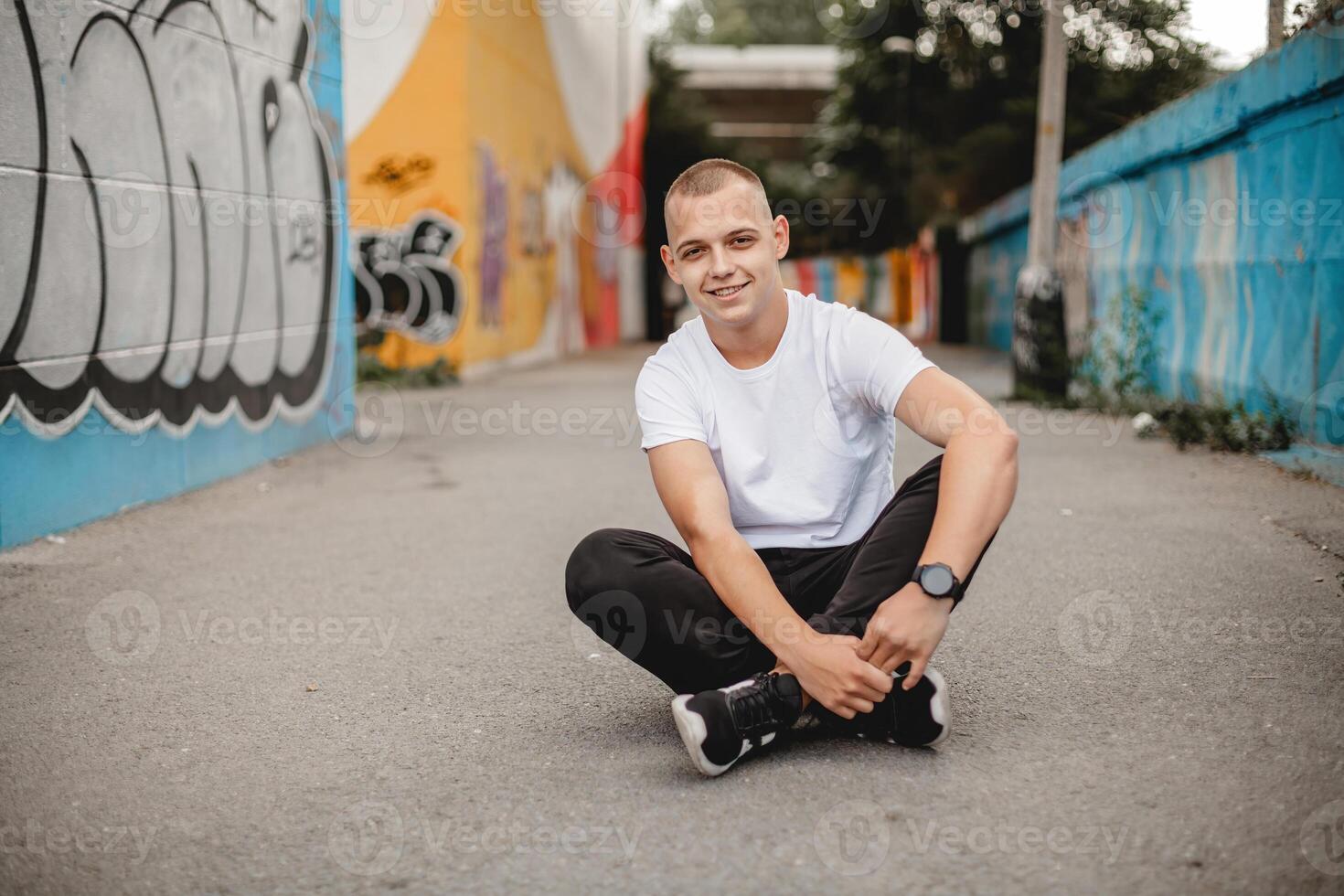 sorridente homem sentado ao ar livre, mãos em joelhos - casual retrato do feliz masculino em chão, sorridente às Câmera - ao ar livre estilo de vida conceito, positivo expressão, relaxado pose - natural luz fotografia foto