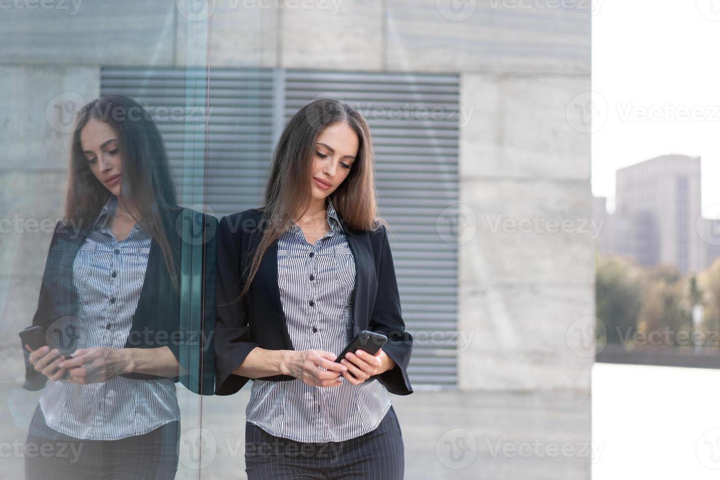 o negócio mulher 35 anos vestido listra camisa e Preto Jaqueta com grandes cabelo em pé perto escritório construção ao ar livre usar Smartphone foto