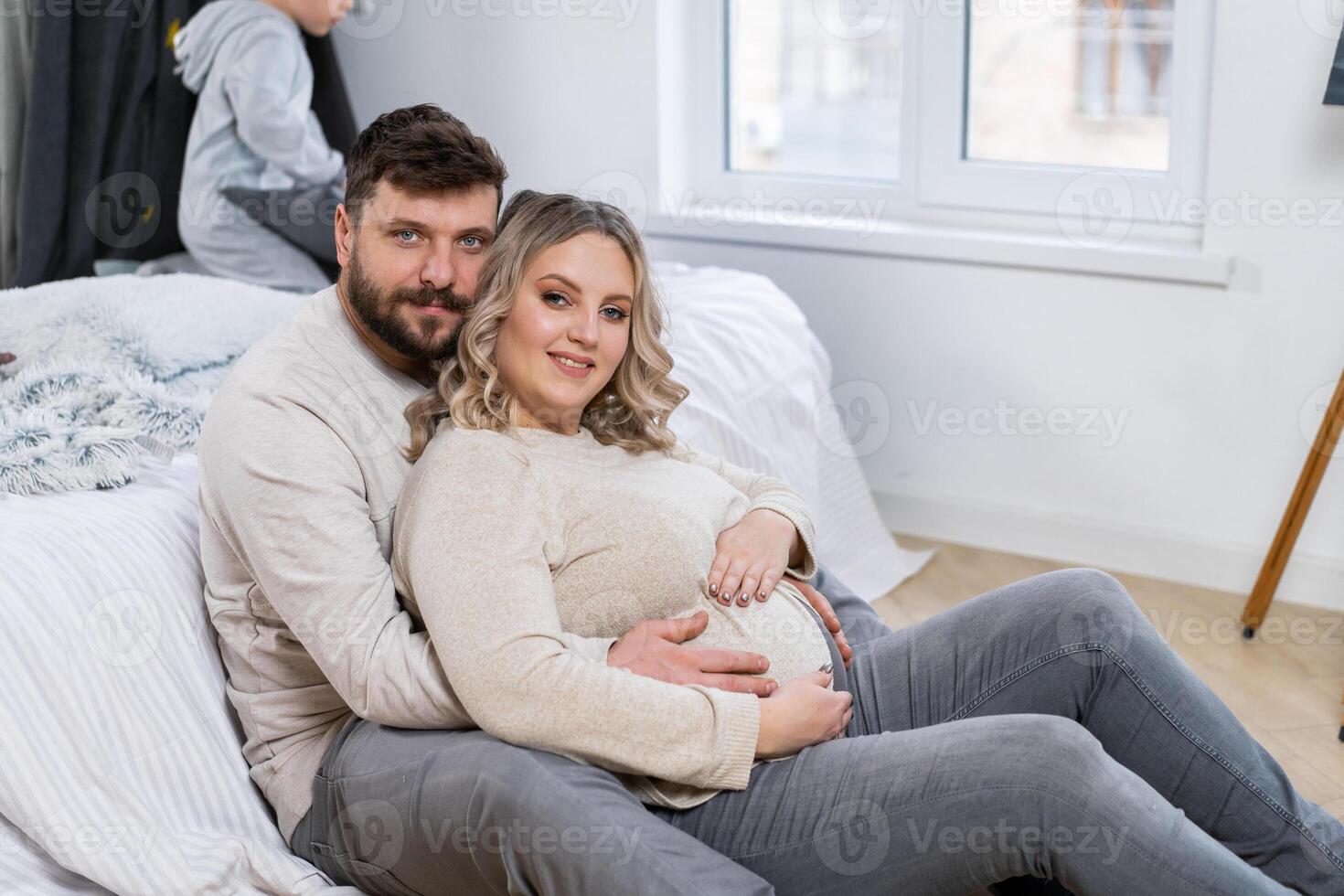 feliz família conceito. marido abraço barriga grávida esposa sentado chão interior vivo quarto perto sofá foto